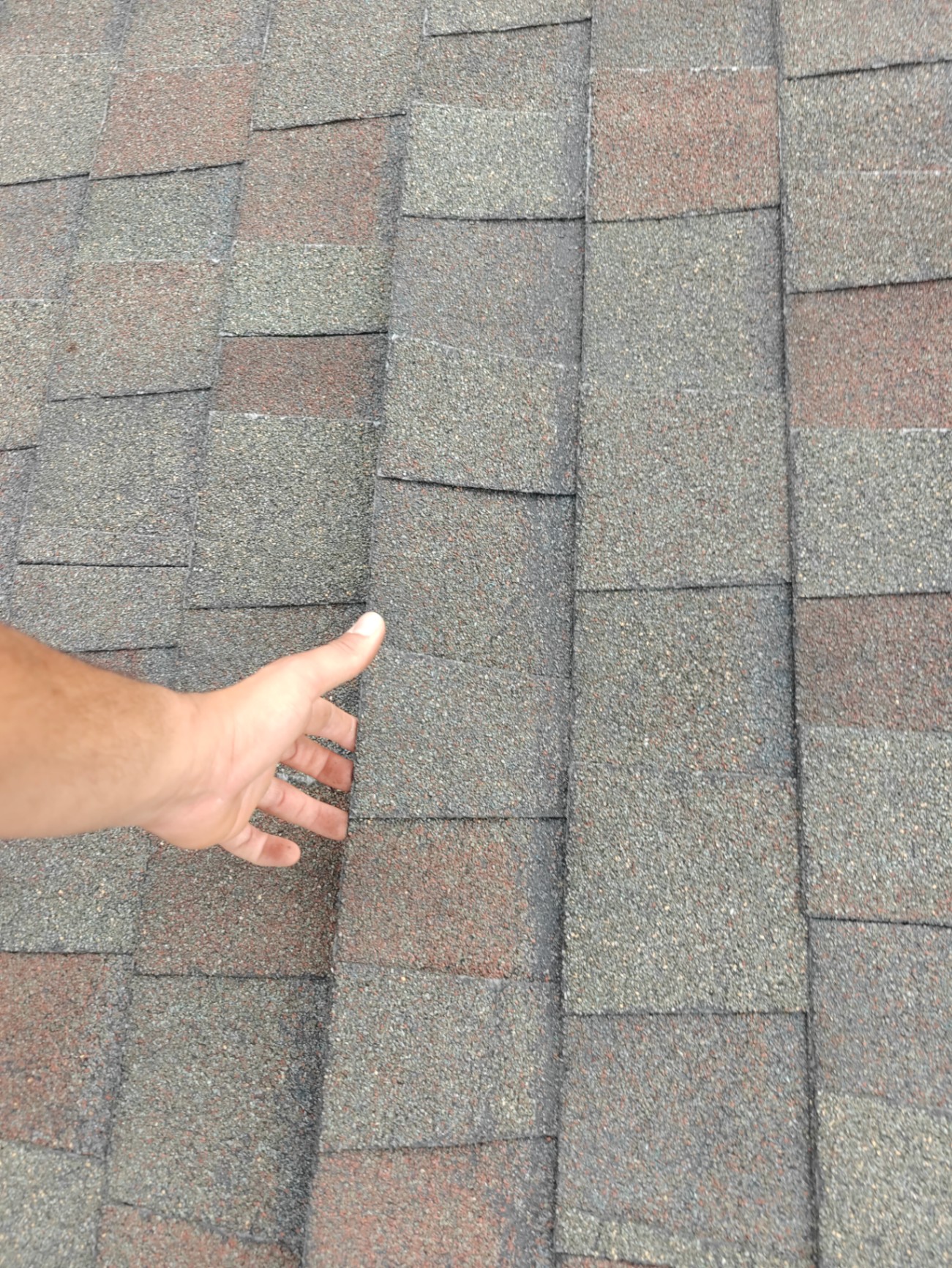 Hand under a lifted shingle showing a broken seal