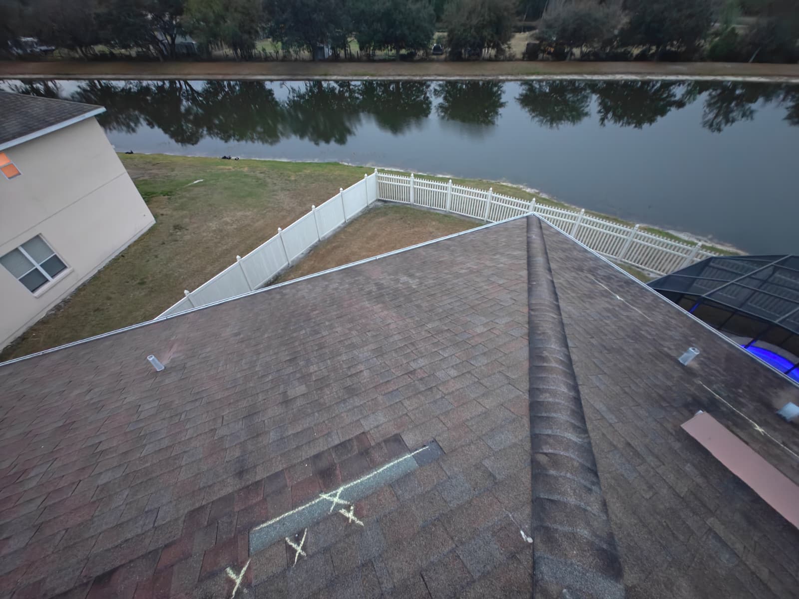 Lakeside home roof with chalk-marked storm damage awaiting replacement