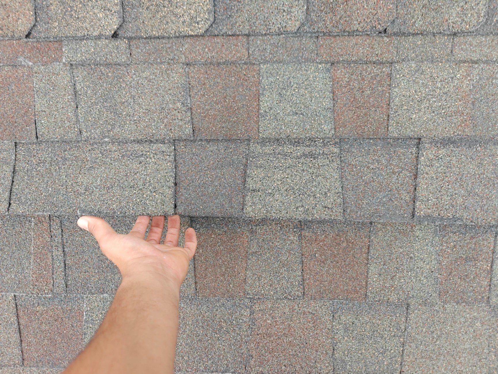 Hand lifting a damaged shingle to reveal storm damage underneath