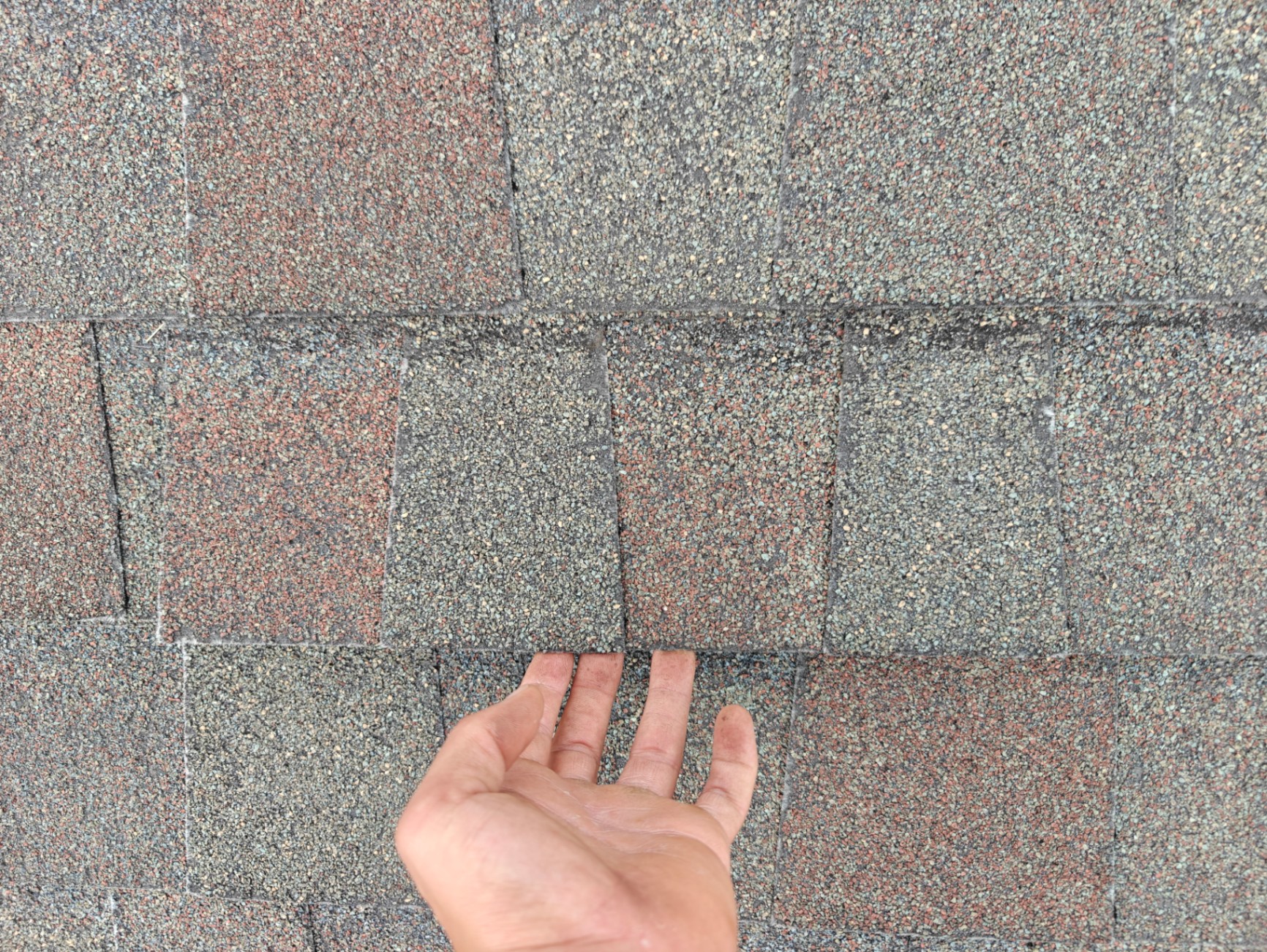 Roofer's hand pointing to wind-creased asphalt shingles
