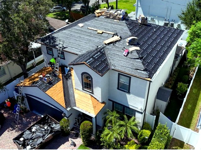 Crew installing underlayment with old roofing loaded in the dumpster